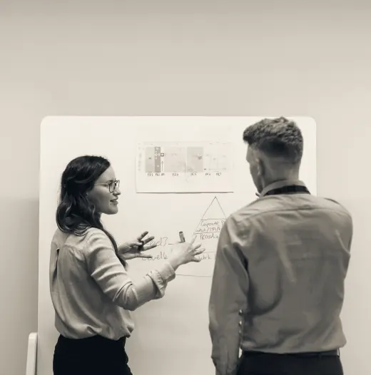 Two colleagues working through a plan at a whiteboard